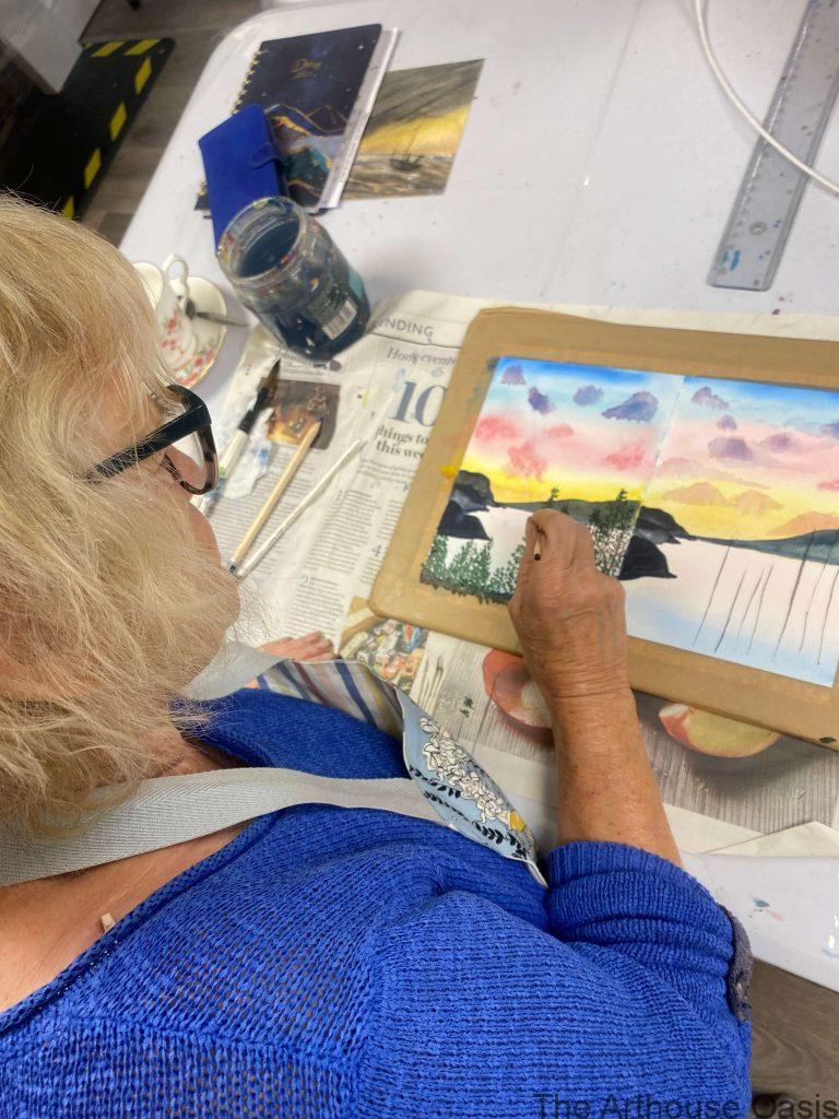 Student painting a colourful sunset landscape in watercolour during a class.