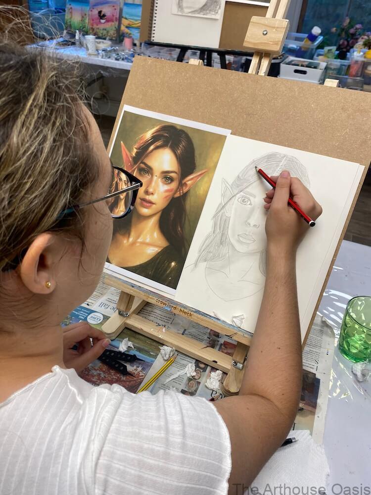 Student at an easel drawing an elf portrait in pencil, with a coloured reference image beside the sketch.
