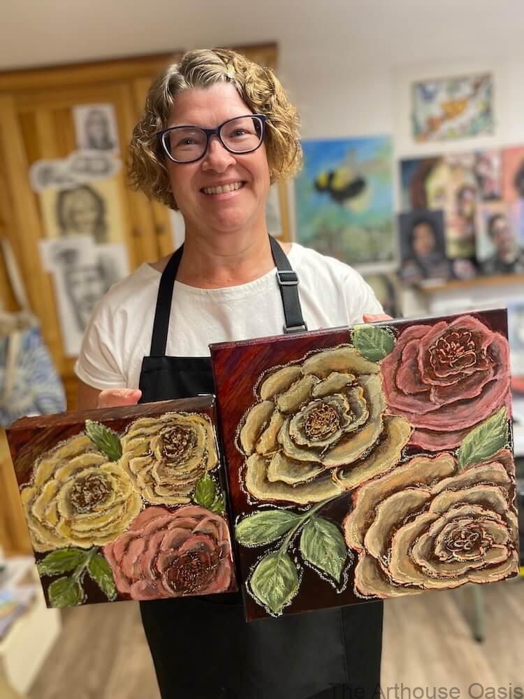 Artist holding two oil paintings of roses in yellow and pink.