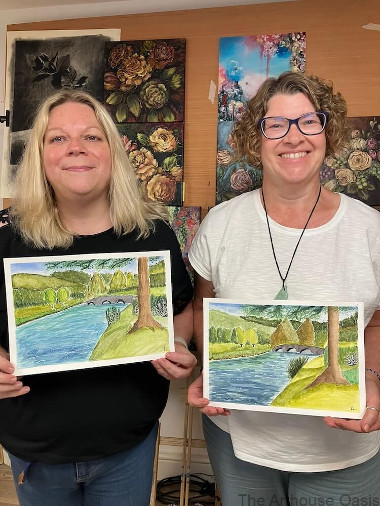 Two smiling students holding their completed watercolour river paintings after class