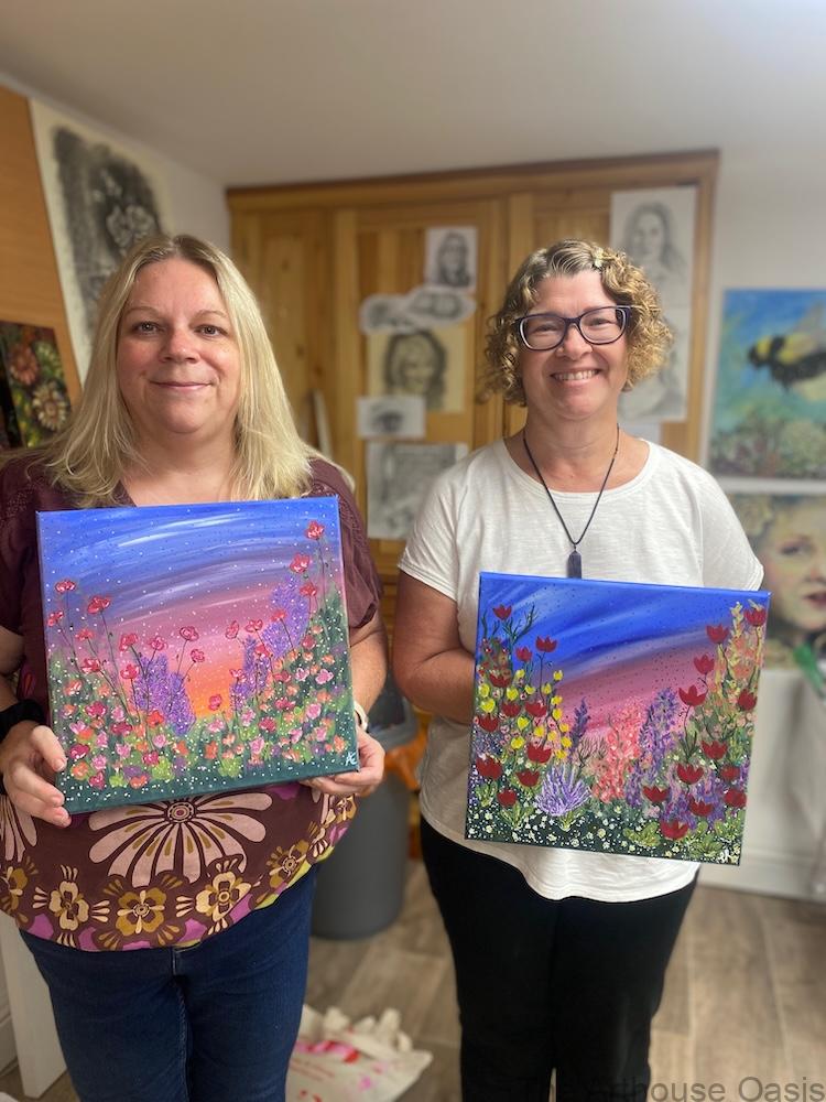 Two women proudly holding up their colourful acrylic wildflower paintings.