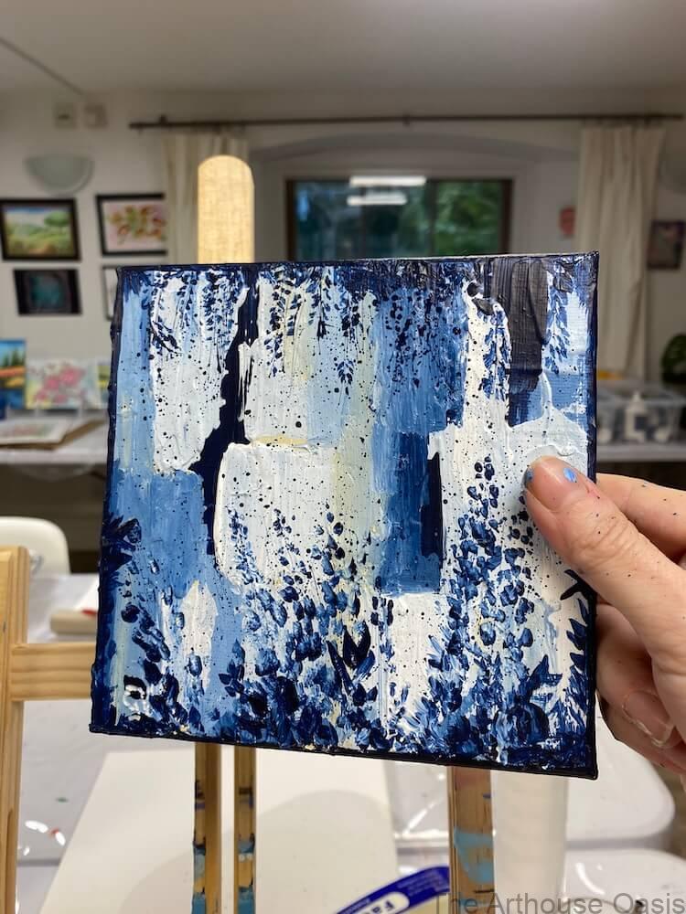 Close-up of a small abstract acrylic painting held in hand, showing layered blue and white textures.