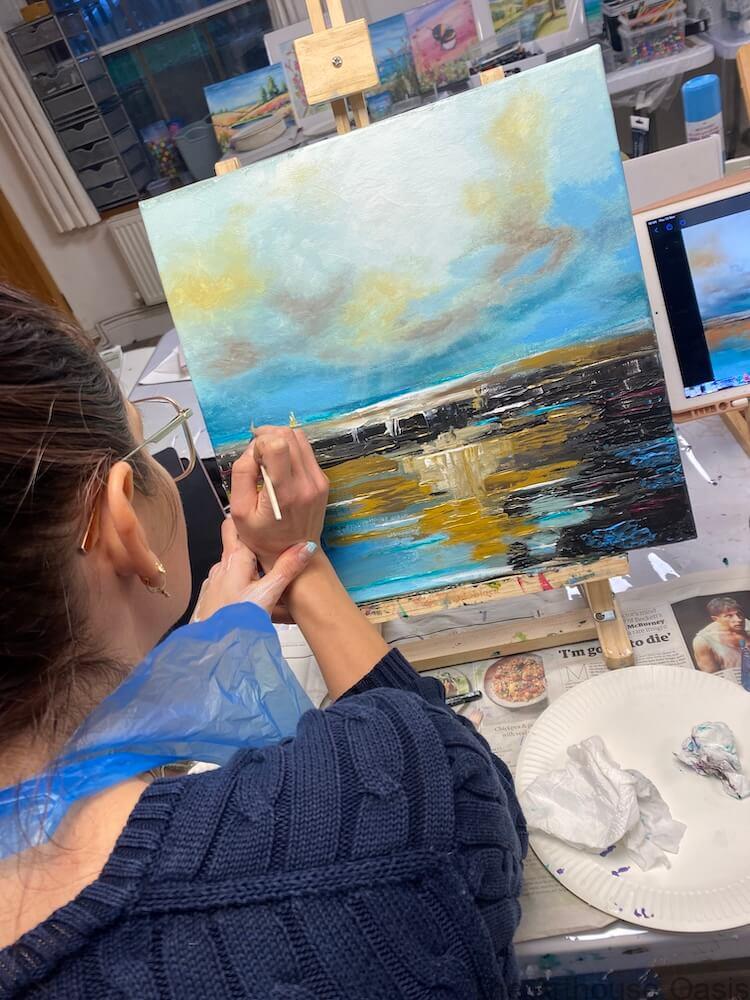 Art student painting an abstract acrylic canvas with palette knives during a guided art lesson.