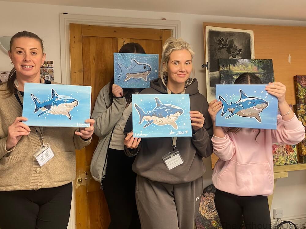 Art students holding finished shark acrylic paintings at the end of a fun painting workshop.