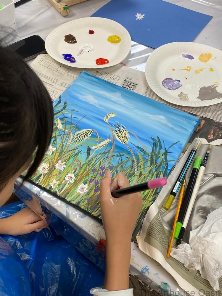 Student painting a coastal acrylic scene with grasses and sea during an art class.
