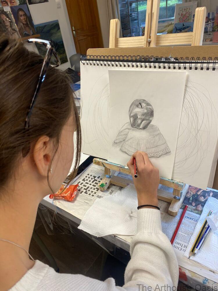 A 14-year-old art student drawing an apple in pencil during an observational drawing session.