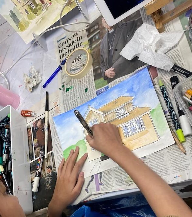Young student working on a watercolour and ink house illustration during a mixed media art session.