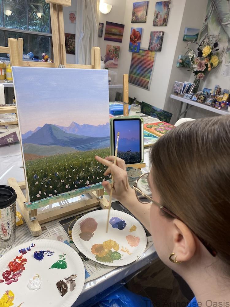 Acrylic landscape painting in progress showing distant mountains and a wildflower meadow.