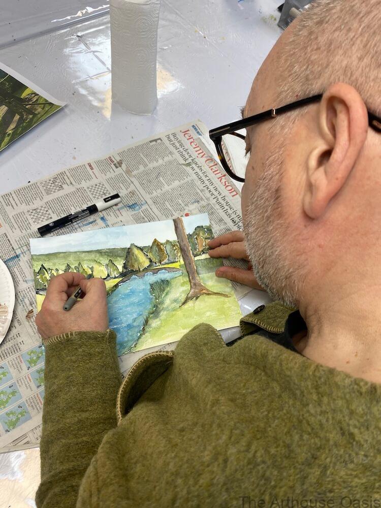 Adult student painting a watercolour river landscape with trees and bridge during an art class in Bishop’s Stortford.