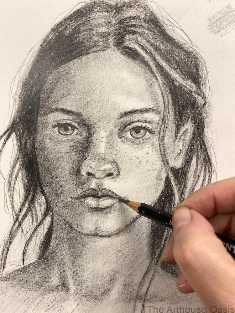 Student refining the lips on a graphite portrait during a pencil drawing class.