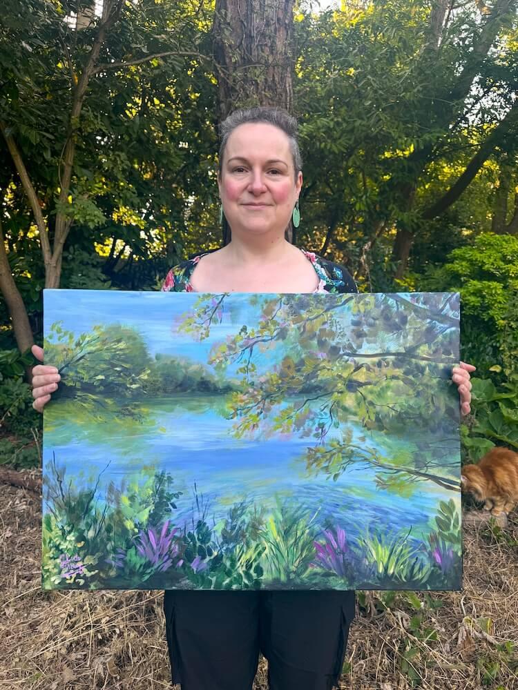 Artist Gabrielle Vickery holding her original acrylic landscape painting 'Hatters Farm Lake' inspired by Hatters Farm in Bishop's Stortford